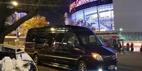 A black Mercedes Sprinter van parked at night with an inset showing the white leather interior seating.