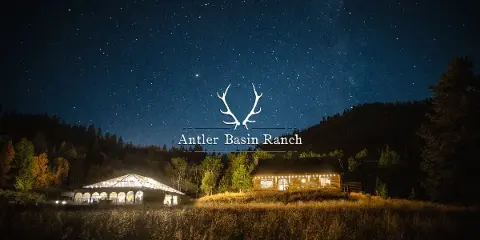 A night view of a rustic log cabin and a large white event tent on a grassy field under a starry sky.