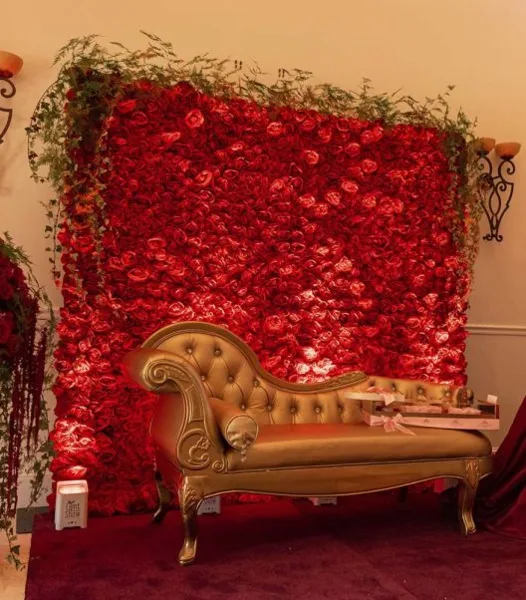 A gold chaise lounge positioned in front of a large red flower wall backdrop.