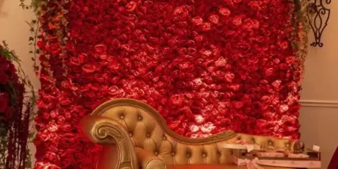 A gold chaise lounge positioned in front of a large red flower wall backdrop.