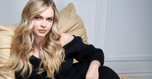 Portrait of a woman with long, styled blonde wavy hair seated on a tan leather chair.