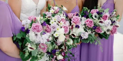 Close-up of a bridal bouquet and bridesmaids' bouquets featuring pink roses, white calla lilies, and purple accents.