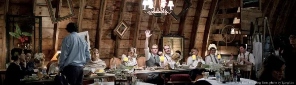 Interior of a rustic wooden wedding barn with a chandelier and a long reception table set for guests.