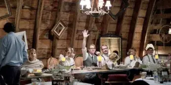 Interior of a rustic wooden wedding barn with a chandelier and a long reception table set for guests.