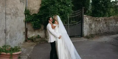 A bride and groom embracing in a rustic outdoor setting with a long veil.