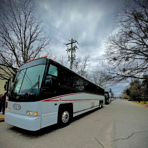 A white and black coach bus with an SLS logo parked on a street, with additional buses visible in the background.