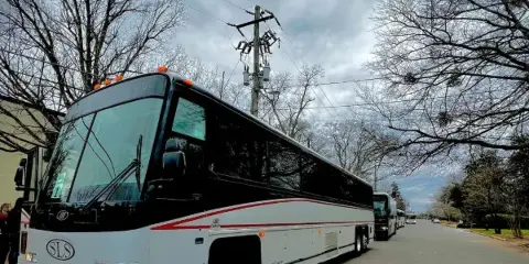 A white and black coach bus with an SLS logo parked on a street, with additional buses visible in the background.