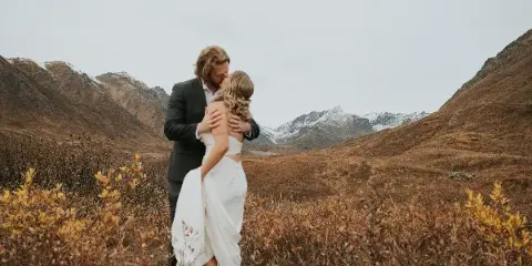 A bride and groom embracing in a mountainous field with snow-capped peaks in the background.