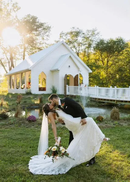 Bride and groom kissing in front of a white open-air chapel at a wedding venue