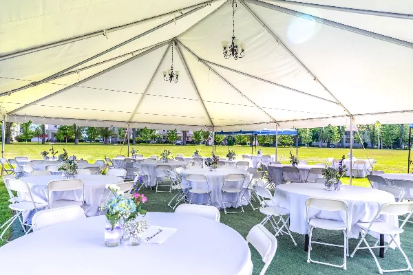 Interior view of a large white event tent set up for a wedding reception with round tables, white chairs, and hanging chandeliers.