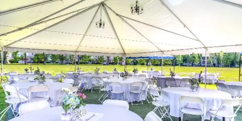 Interior view of a large white event tent set up for a wedding reception with round tables, white chairs, and hanging chandeliers.