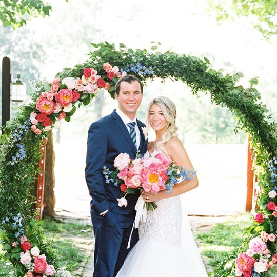 A bride and groom standing together under a floral archway.