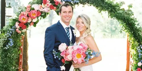 A bride and groom standing together under a floral archway.