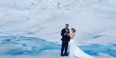 A bride and groom standing on a glacier with snow-covered mountains in the background.