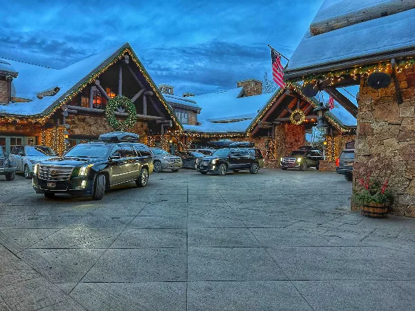 A fleet of black luxury SUVs parked in the driveway of a snow-covered mountain resort lodge.