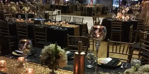 A wedding reception hall set with round tables, gold Chiavari chairs, and floral centerpieces.