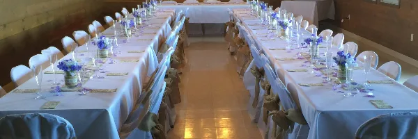 A wedding reception hall with long tables set with white tablecloths, floral centerpieces, and chairs with sashes.