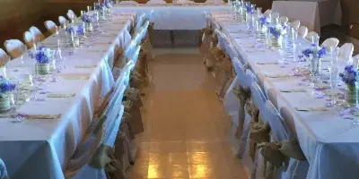 A wedding reception hall with long tables set with white tablecloths, floral centerpieces, and chairs with sashes.