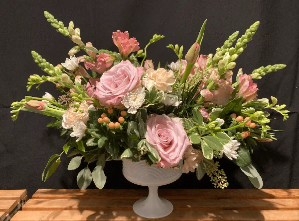 A floral arrangement with pink roses and greenery in a white pedestal vase