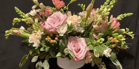 A floral arrangement with pink roses and greenery in a white pedestal vase
