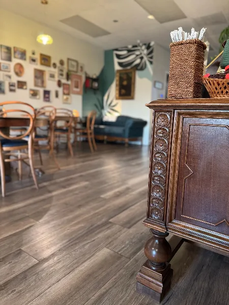 Interior view of a vintage-style café featuring wooden furniture, a display counter, and a wall of framed art.