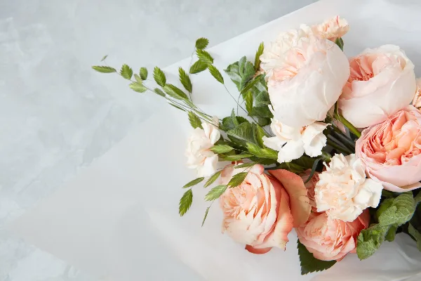 A close-up photograph of a fresh floral arrangement with peach roses and greenery on a white surface.