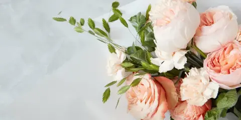 A close-up photograph of a fresh floral arrangement with peach roses and greenery on a white surface.