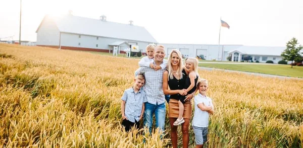 A family posing in a golden field with a large white barn in the background.
