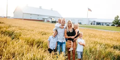 A family posing in a golden field with a large white barn in the background.