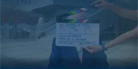 A person holding a film clapperboard in front of a man in a suit, representing a video production set.