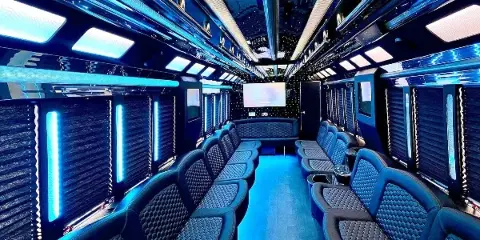 Interior view of a luxury party bus with blue LED lighting and leather seating.