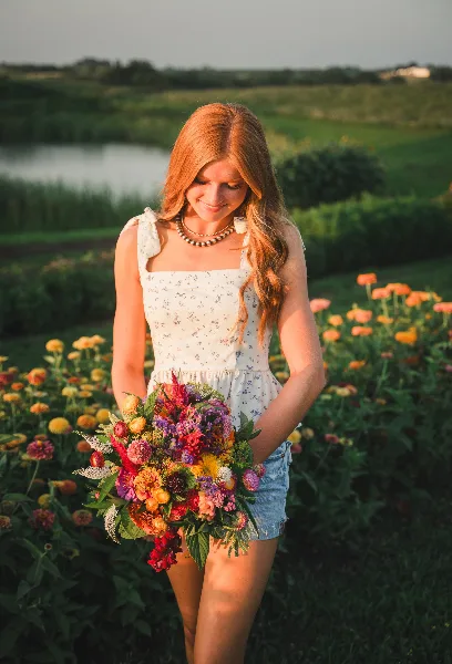 A woman holding a colorful, mixed-flower bouquet in a field of blooming flowers.