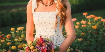 A woman holding a colorful, mixed-flower bouquet in a field of blooming flowers.