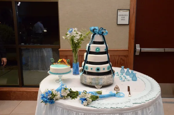 Wedding table with a tiered blue and black cake, small cake, floral arrangements, and table decorations.