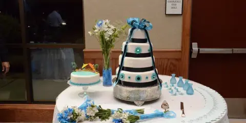 Wedding table with a tiered blue and black cake, small cake, floral arrangements, and table decorations.