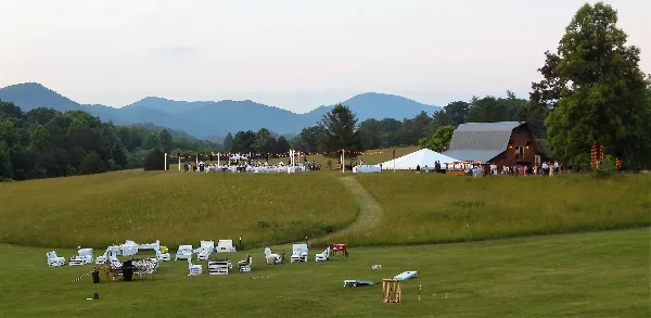 A wide shot of a wedding venue featuring a barn, outdoor reception area with string lights, and a mountainous landscape in the background.