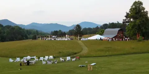 A wide shot of a wedding venue featuring a barn, outdoor reception area with string lights, and a mountainous landscape in the background.