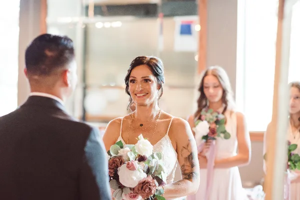 Bride in white dress holding a floral bouquet smiling at the groom during a wedding