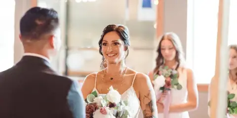 Bride in white dress holding a floral bouquet smiling at the groom during a wedding