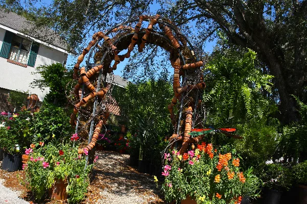 Outdoor garden area featuring a decorative arch, potted plants, and flowers at a florist shop.