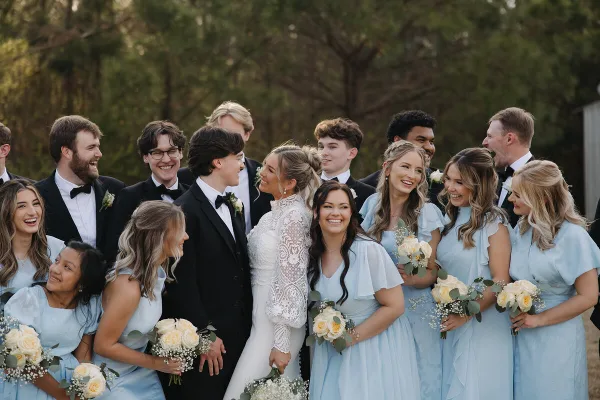 A wedding party including the bride, groom, and attendants posing outdoors with bouquets.