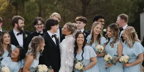 A wedding party including the bride, groom, and attendants posing outdoors with bouquets.