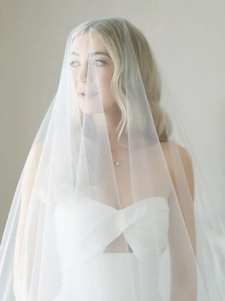A bride with styled hair and makeup wearing a white dress and veil.