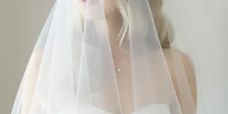 A bride with styled hair and makeup wearing a white dress and veil.
