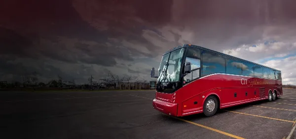 A red CIT Signature Transportation motorcoach parked in a lot under a cloudy sky.