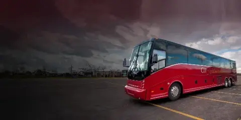 A red CIT Signature Transportation motorcoach parked in a lot under a cloudy sky.
