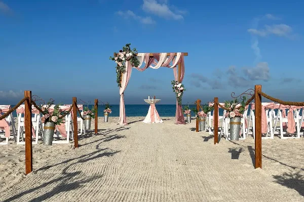 A beach wedding ceremony setup with a floral arch, white chairs, and aisle decorations on the sand.