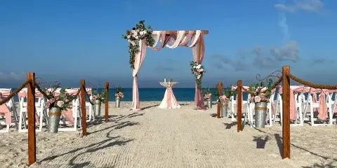 A beach wedding ceremony setup with a floral arch, white chairs, and aisle decorations on the sand.