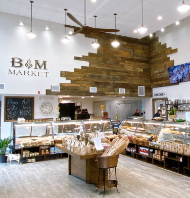 Interior view of B&M Market showing the service counter, display cases, and rustic wood wall decor.