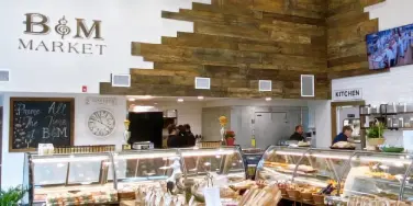 Interior view of B&M Market showing the service counter, display cases, and rustic wood wall decor.